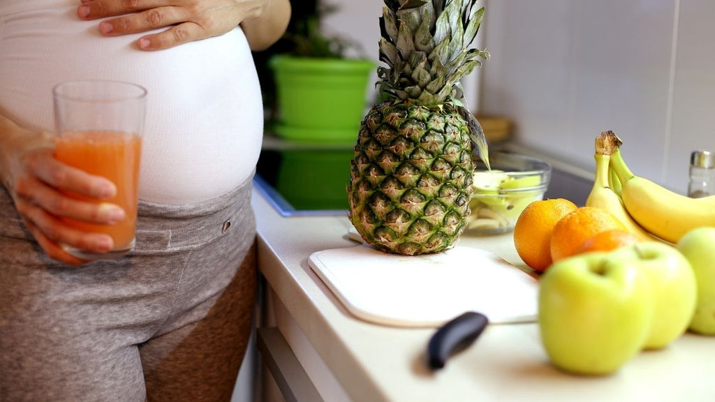 pregnant woman with fruits on table and fruit juice in hand
