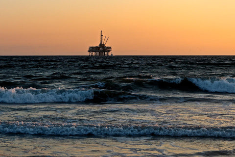 Oil rig in the ocean. There is a sunset or sunrise behind the rig and waves crashing against the shore 