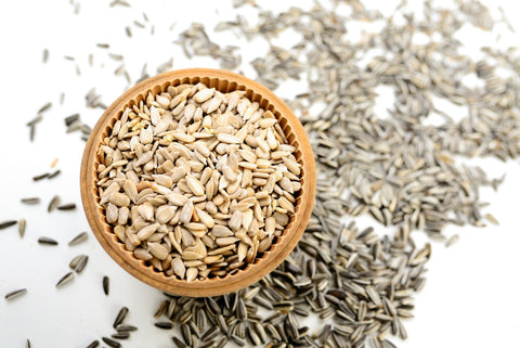 Small bowl with shelled sunflower seeds surrounded by unhulled seeds below on the table