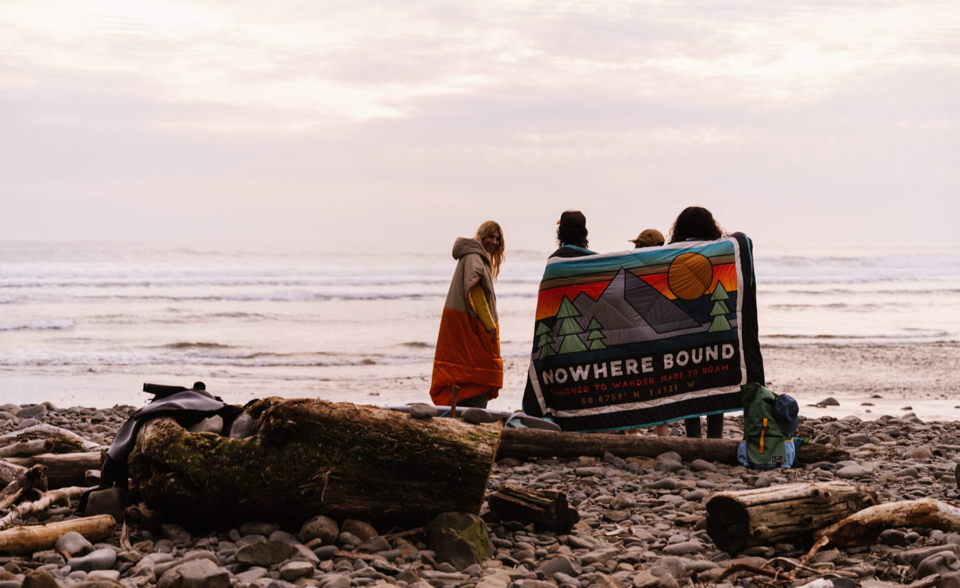 A group of friends looking out to sea wrapped in a nomadic blanket.