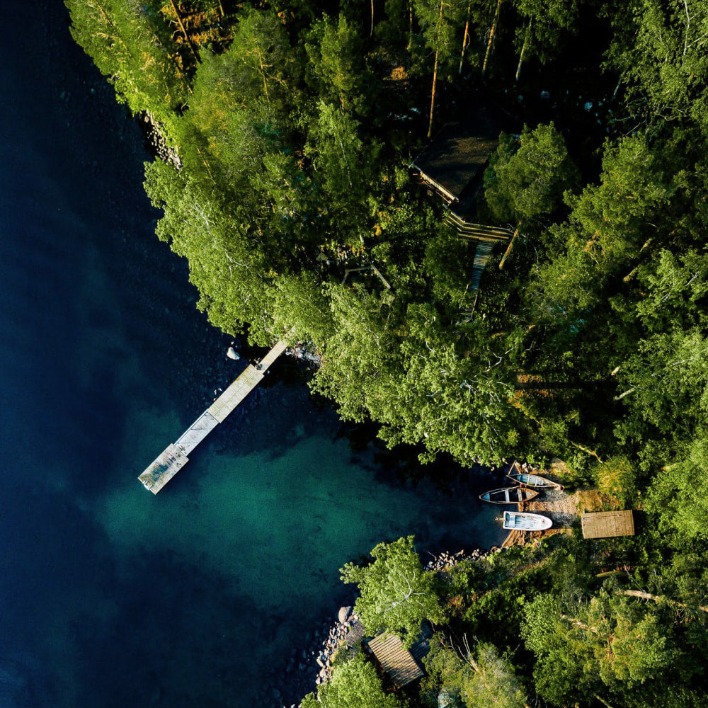 A top down view of a forest coastline, with pontoon extending out into the water, with boats nearby