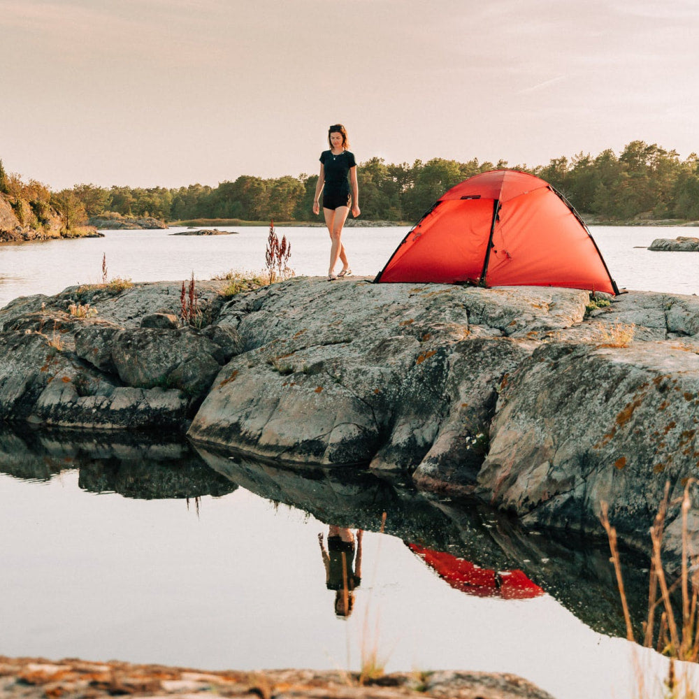 A person and their dog pitch a tent next to a still pool of water.