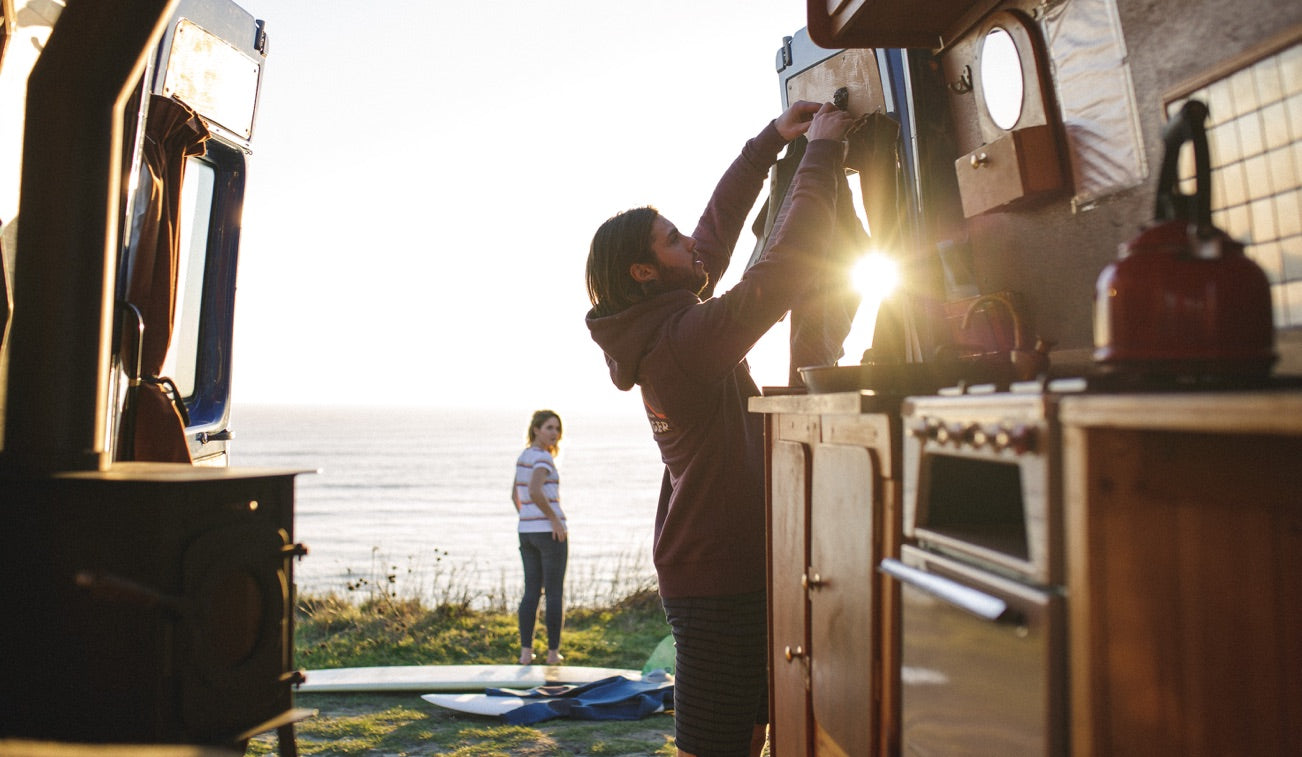 A couple enjoy a sunset view over the ocean fromm their quirky camper