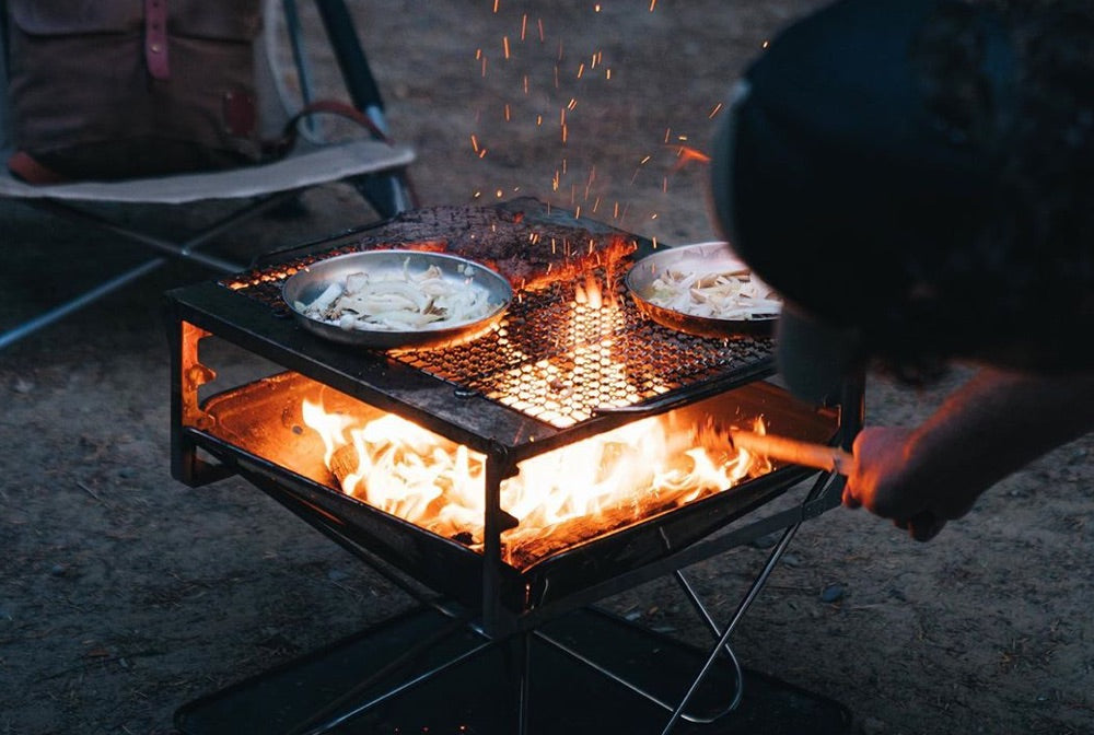 A campfire grill is cooking away with a roaring fire