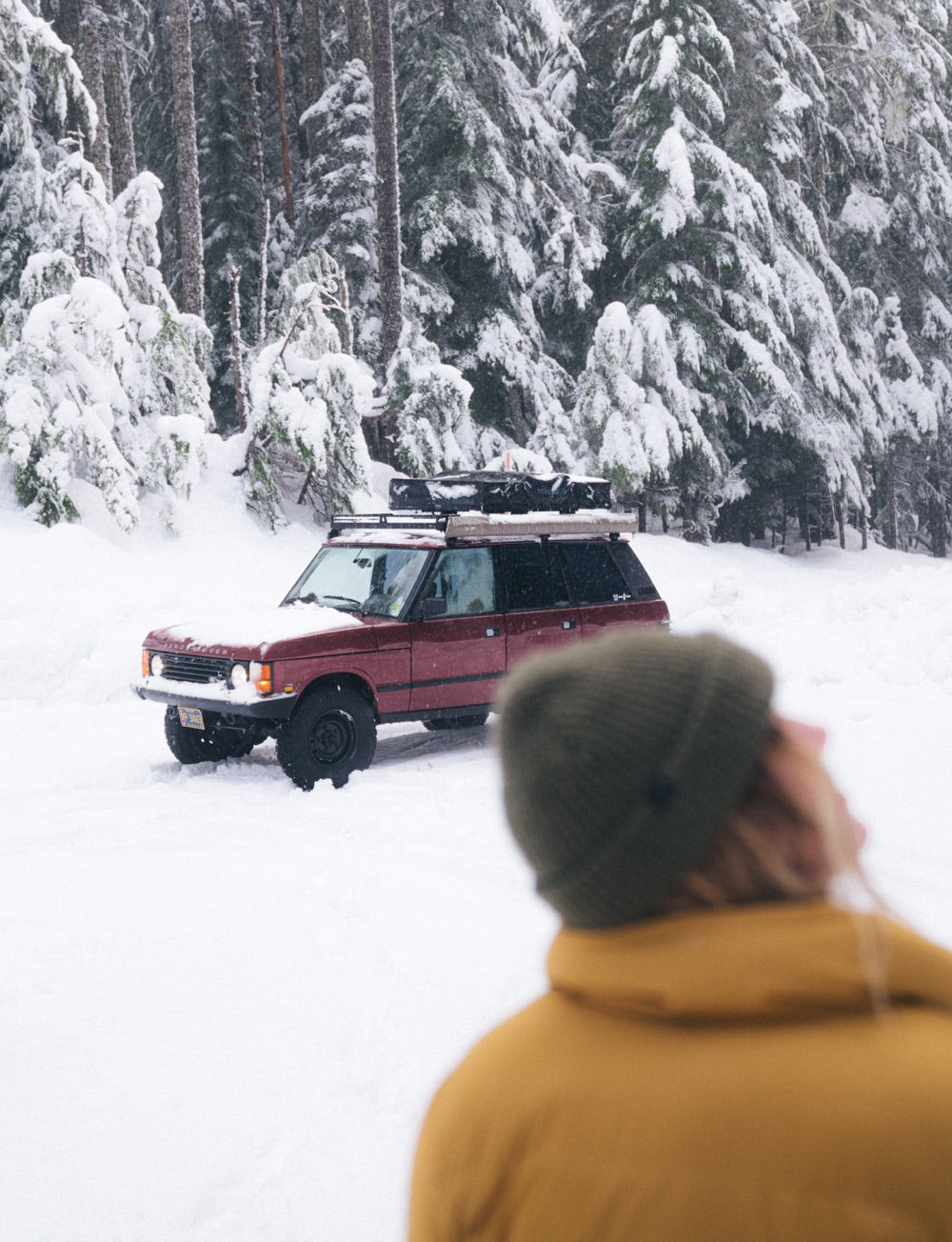 A 4x4 drives through a snow covered road in a forest.