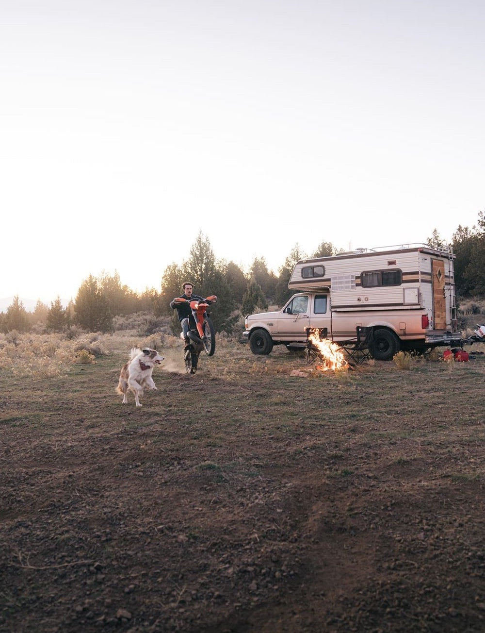 A man wheelies a motorcross bike while an excited dog gives chase