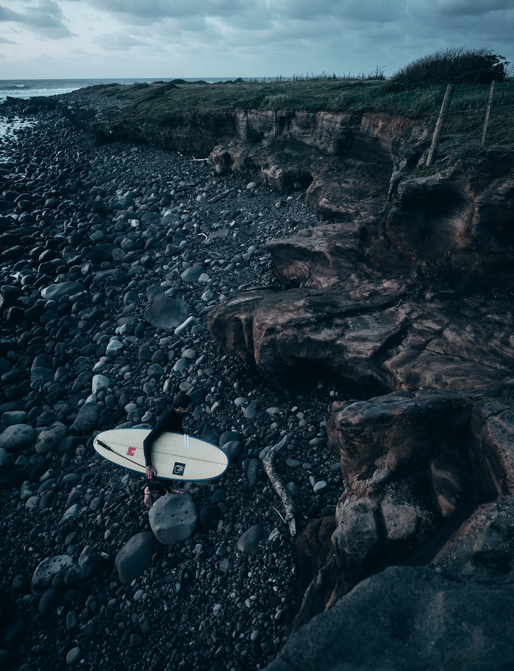 A surfer exits the water ready to scramble up the rocks to the field above