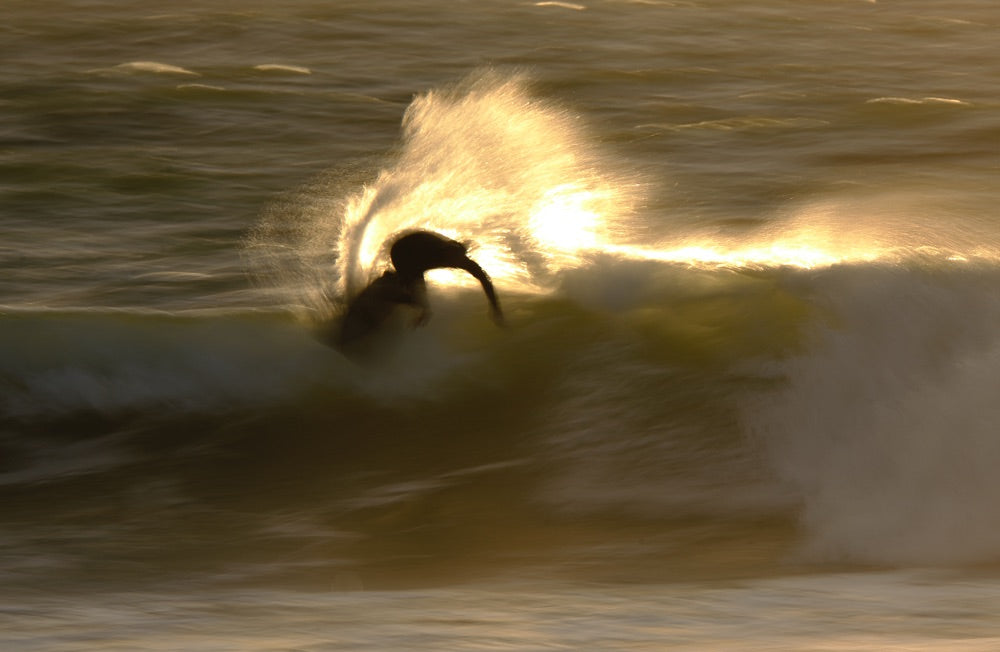 Sense of adventure: A blurry photo of a surfer a they perform a top turn on a wave, throwing water spray behind them