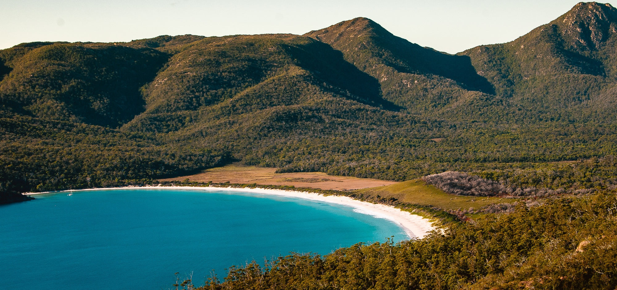 Wineglass Bay - A beautiful white sand beach surrounded by mountains and hills covered in trees with a brilliant blue sea rolling in to the shore.