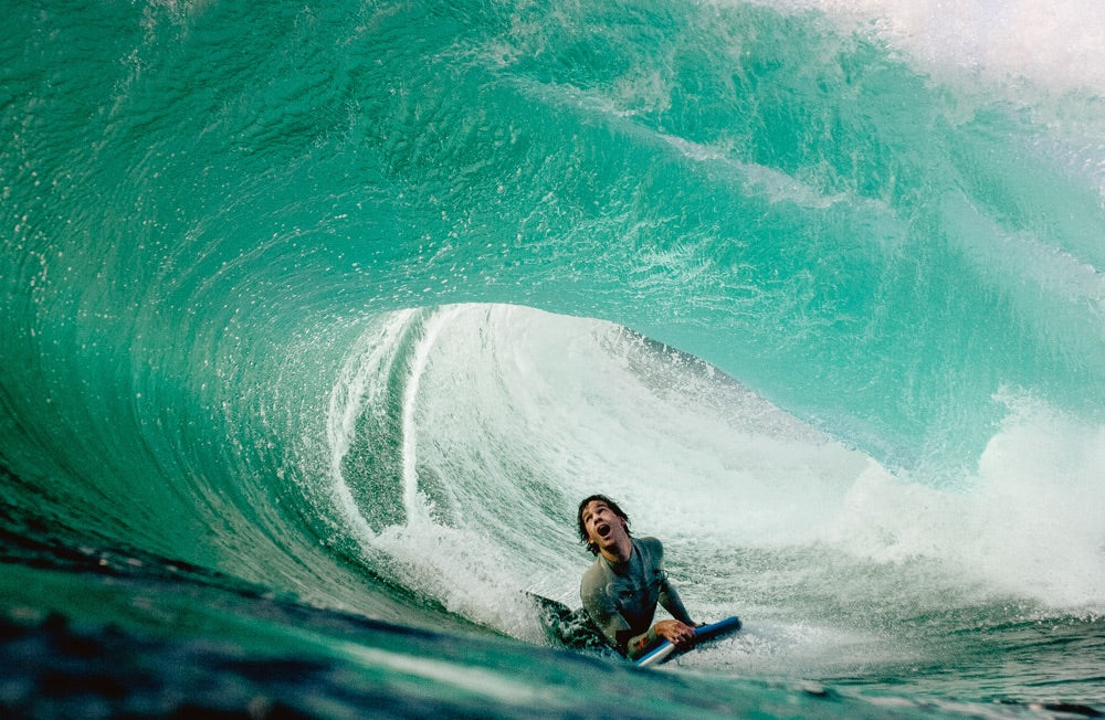 A bodyboarder looks up in awe as a barrelling wave breaks over the top of him.