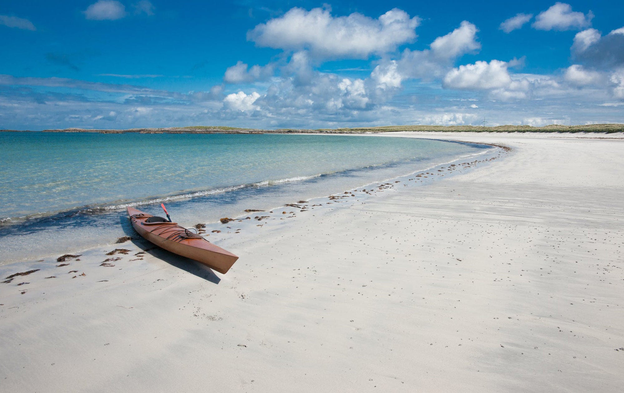 A lone kayak sits in front of blue water and white sands.