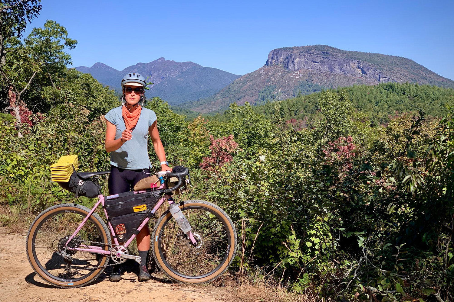 A woman stands by her bike on a mountain path