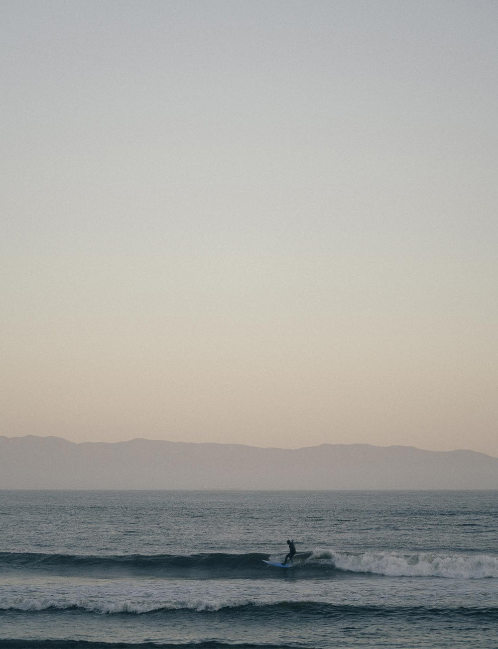 A lone surfer rides the last wave of the day with a hazy dusk horizon in the background