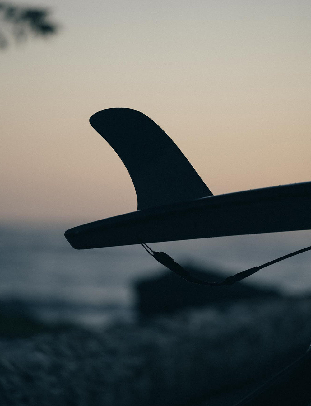 Silhoette of a single-fin longboard surfboard with a dusky sunset background.
