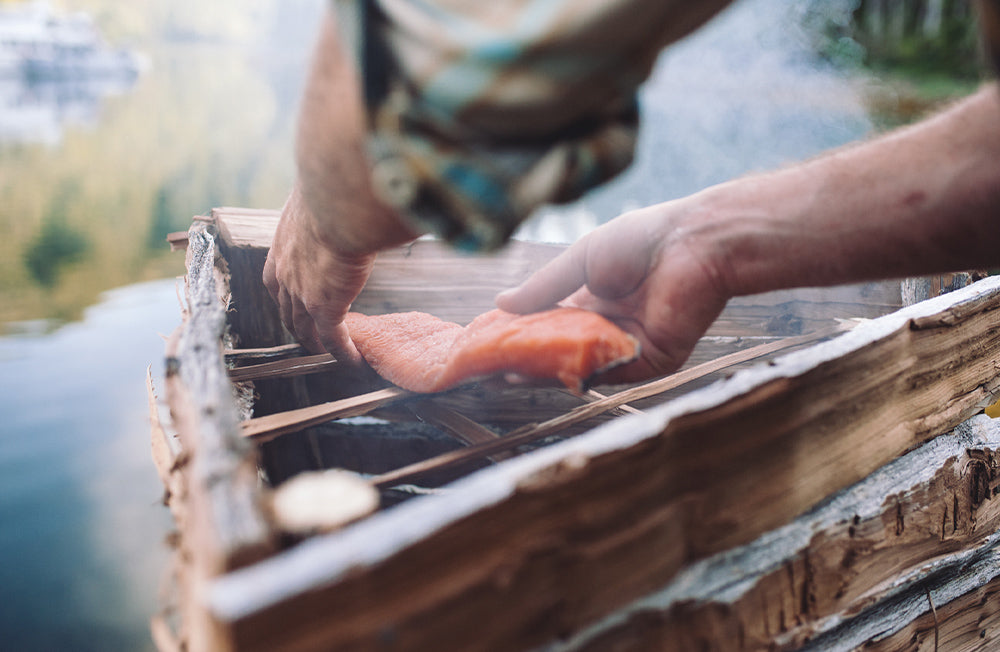 A man smokes freshly caught salmon on a traditional smoker