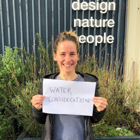 Green&Blue team member Annie holding a sign that says water consideration stood outside the workshop