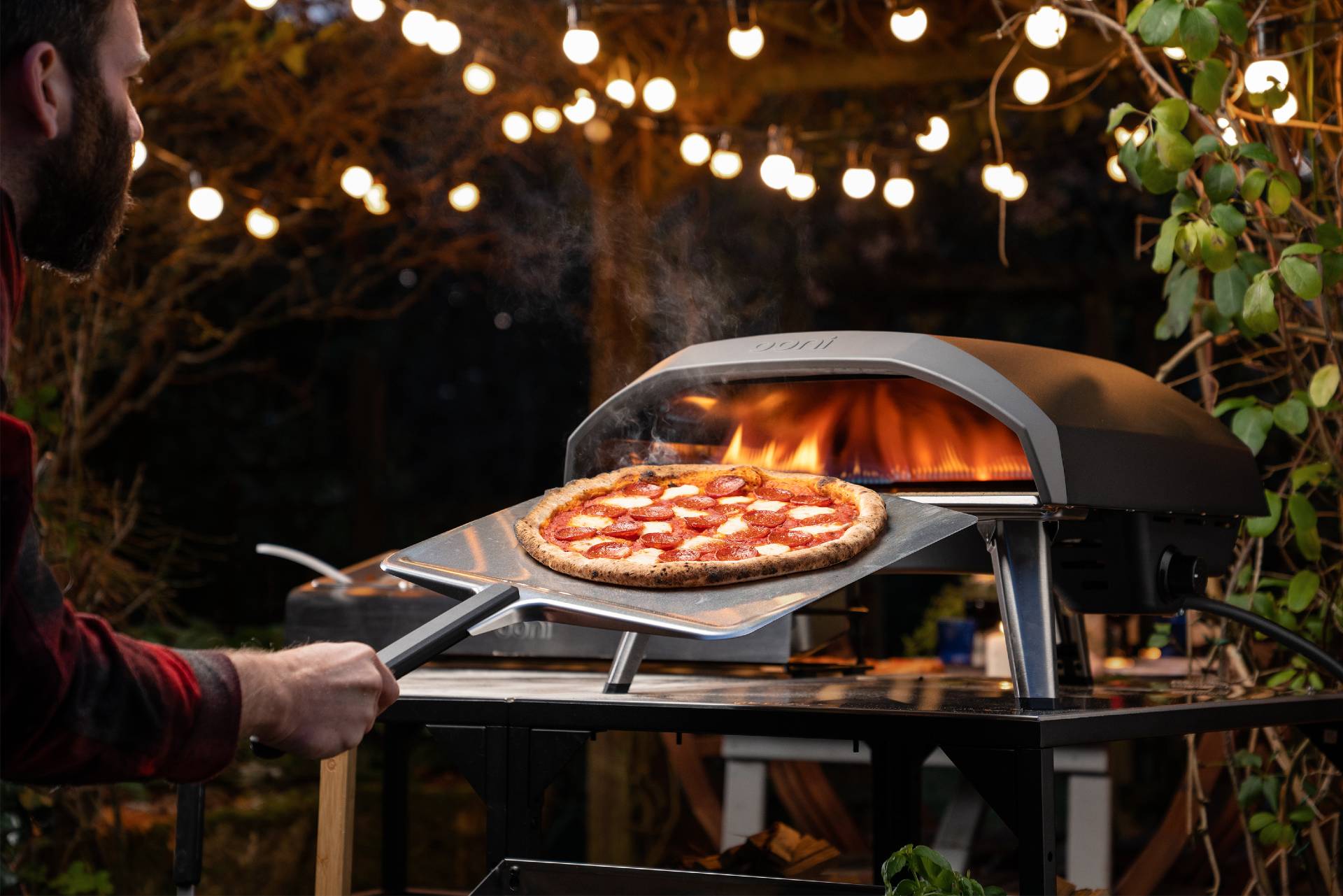 A man using an aluminium pizza peel to place a pizza into an Ooni Pizza Oven