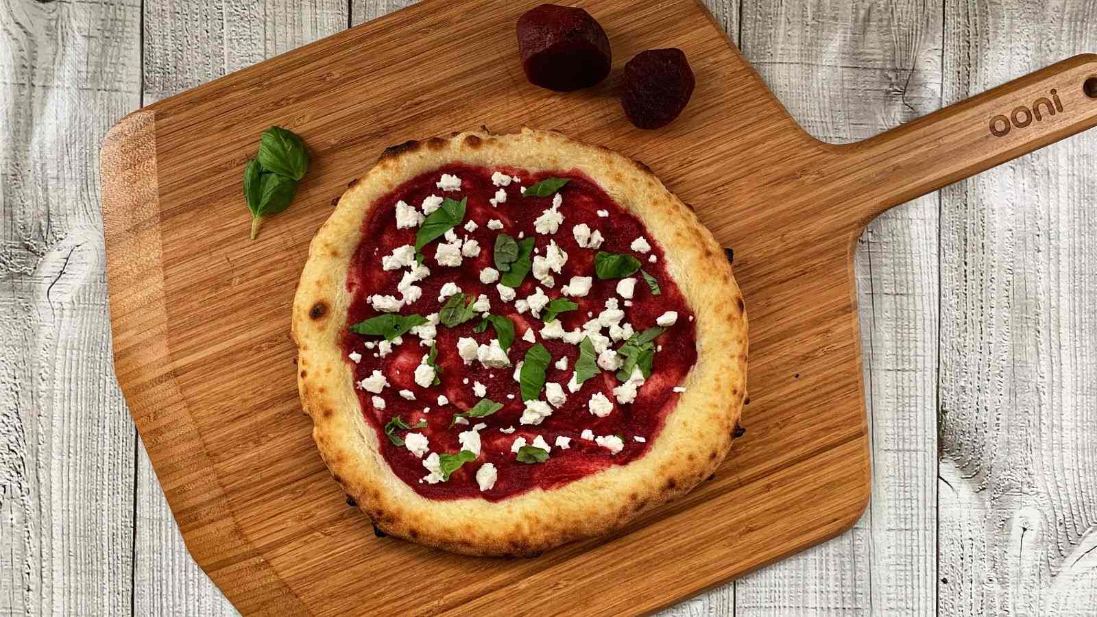 Cooked biga dough pizza with beetroot, feta and basil on an Ooni Bamboo Serving Board & Pizza Peel.