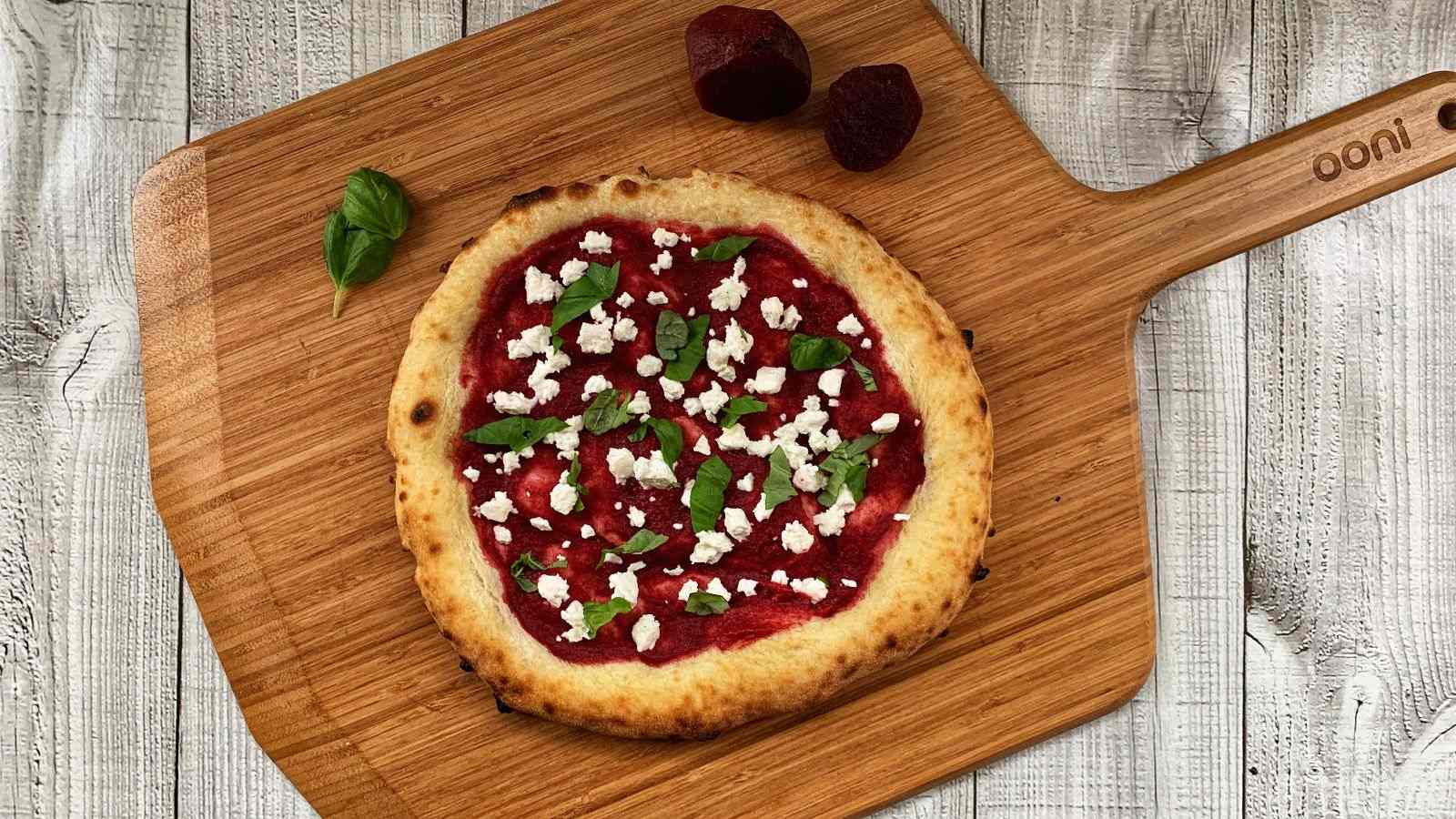 Una pizza con impasto biga, condita con barbabietola, feta e basilico viene servita sulla Pala per pizza & Tagliere in bambù Ooni.