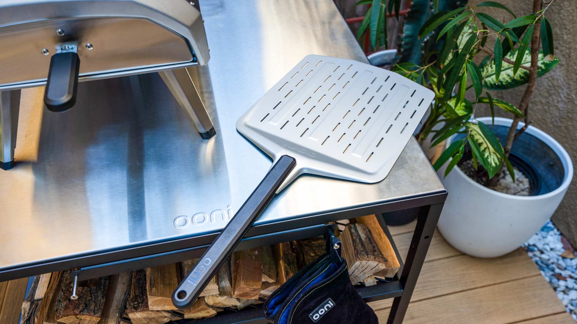 Ooni Perforated Pizza Peel and Ooni Karu 12 on an Ooni Modular Table with wood logs.