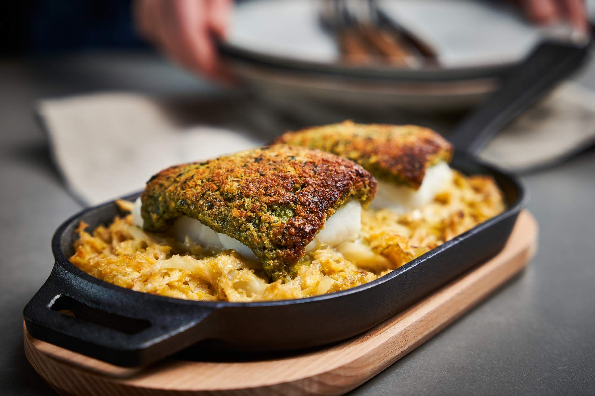 Schlemmerfilet – Herb-crusted cod with creamed Savoy cabbage in an Ooni Cast Iron Skillet Pan on a wooden base on a table.