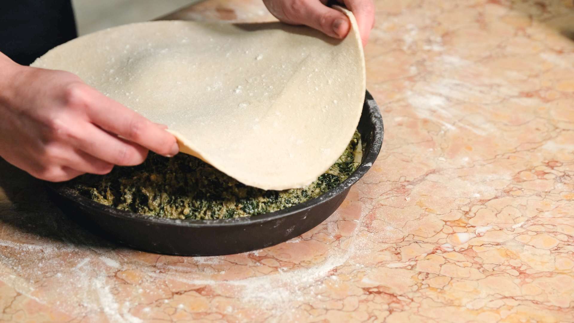 Pastry being placed onto top of a mixture of spinach and cheese in a cake tin