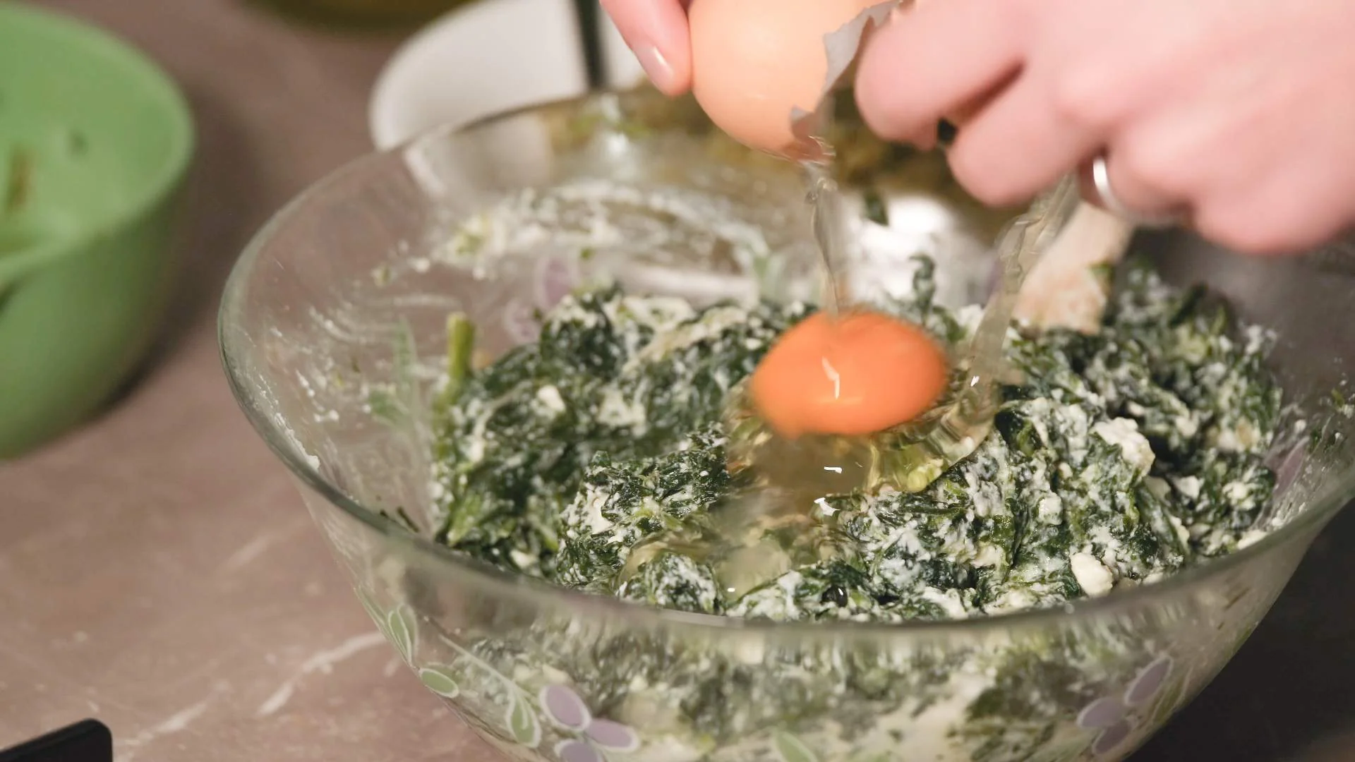 Egg being cracked in a glass bowl full of spinach and cheese