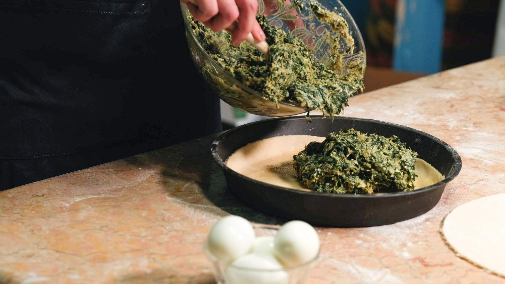 Mixture of spinach and cheese being poured into a cake tin filled with pastry from a glass bowl