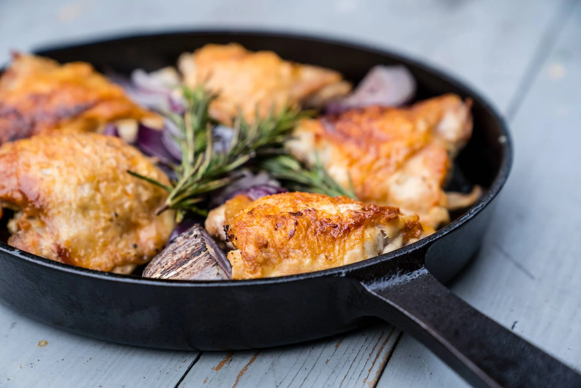 Cooked roasted chicken and onions with sprigs of rosemary in an Ooni Cast Iron Skillet Pan on a table.