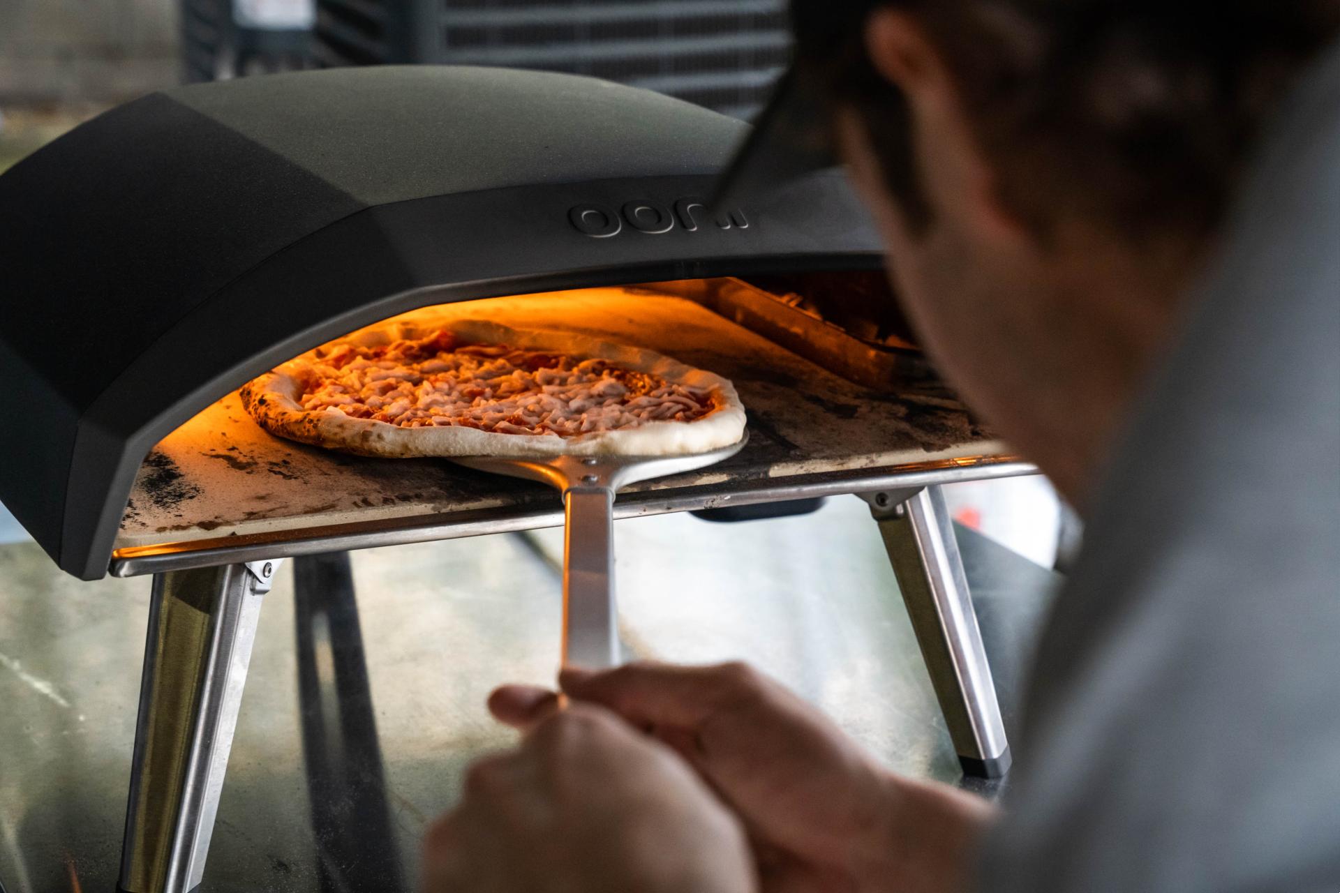 Pizza being put into an Ooni pizza oven with an Ooni pizza peel