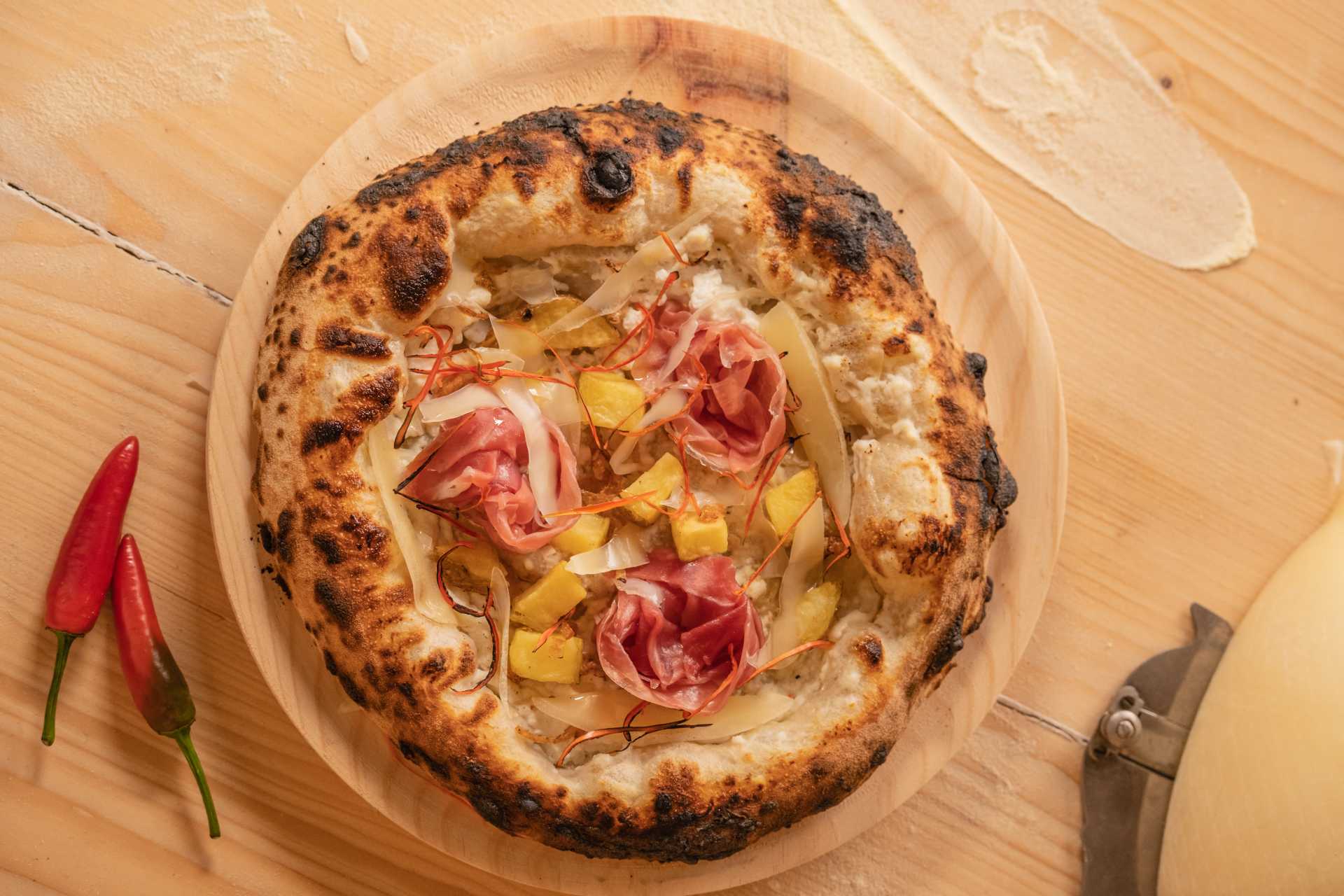 Cooked Calabrese pizza with ricotta, ham, potato, onion and spicy chili pepper pizza on a wooden table.