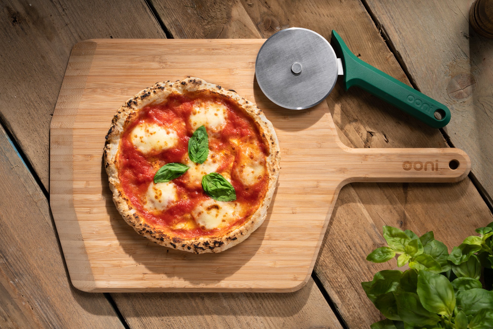 Gluten-free margherita pizza with tomato sauce, mozzarella and basil on an Ooni Bamboo Pizza Peel & Serving Board with an Ooni Professional Pizza Cutter Wheel.