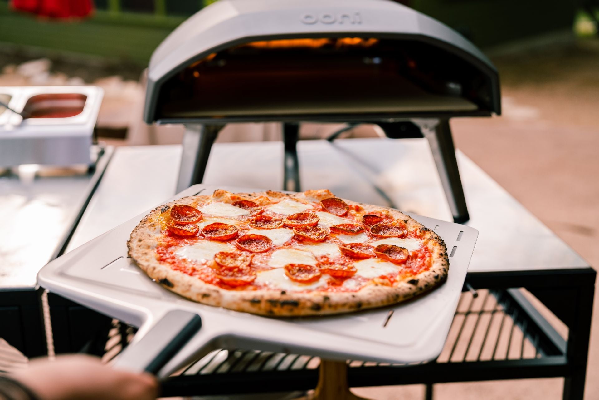 A perforated pizza peel being using to place a pizza into an Ooni pizza oven