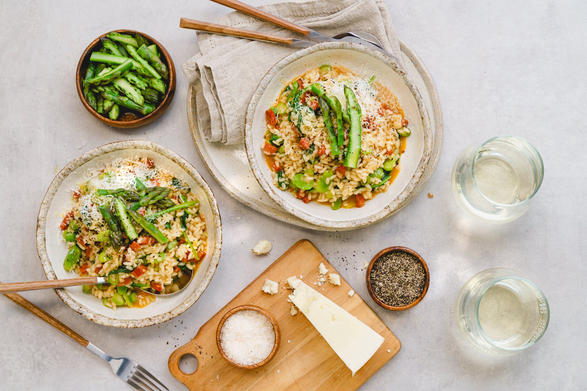 Two bowls of risotto sitting next to a chopping board holding a block of parmesan