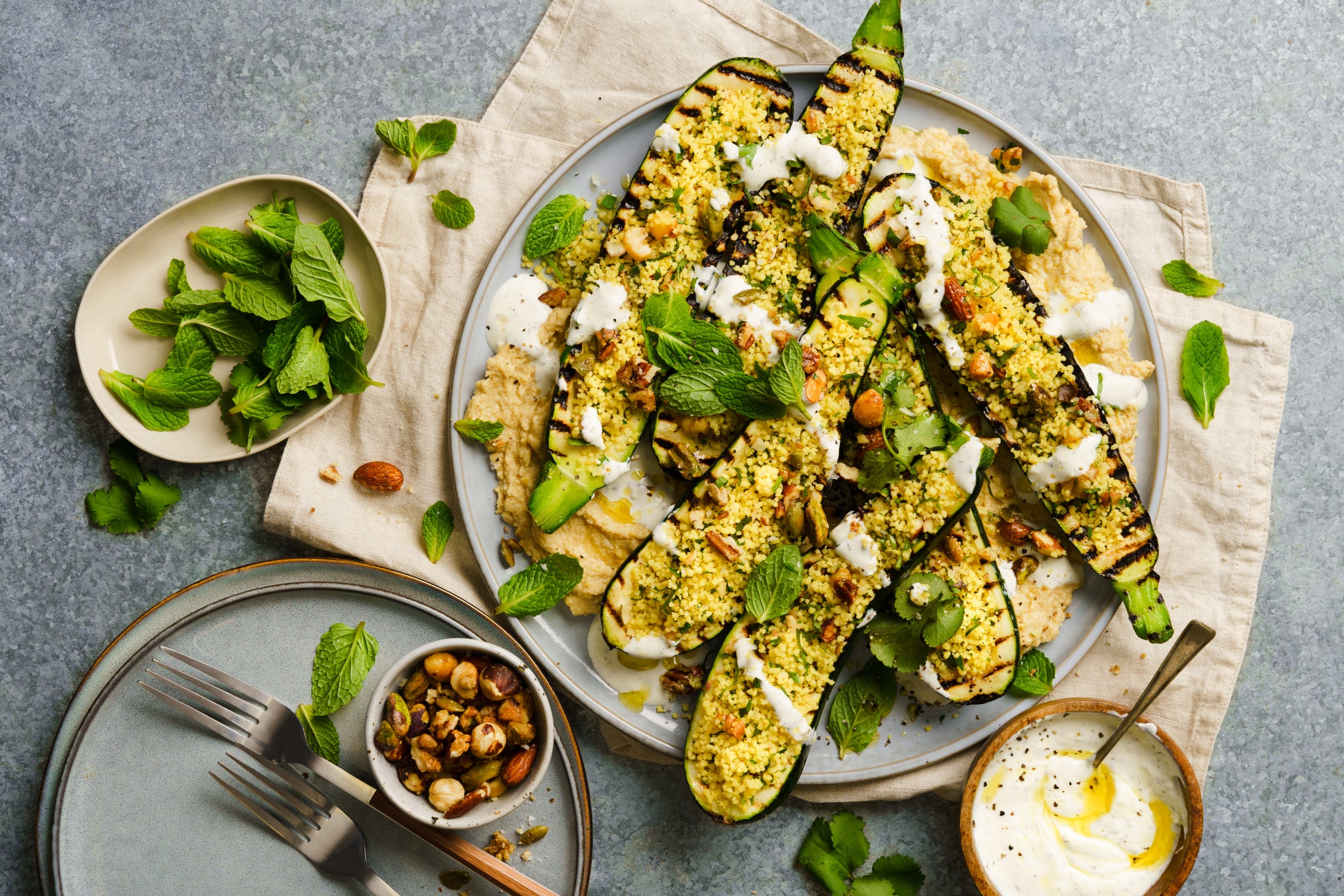 An image of zucchini stuffed with couscous surrounded by little bowls of herbs and yoghurt