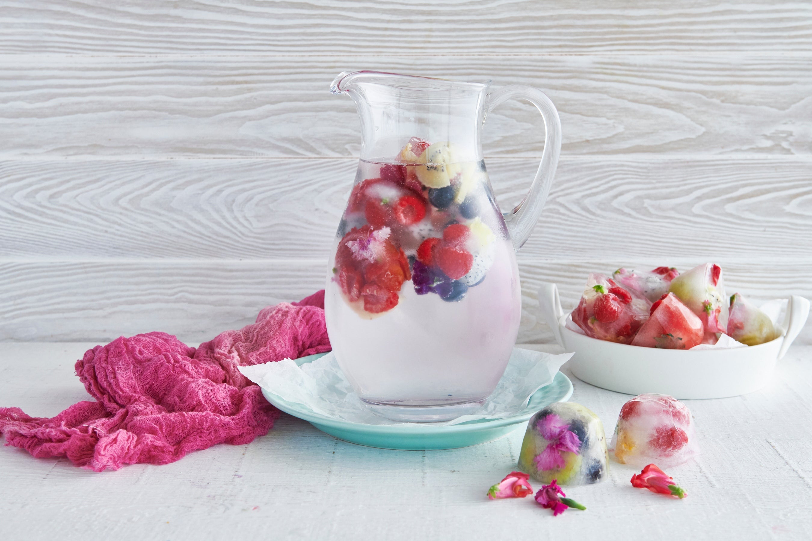 A glass jug of water with fruit and flower ice cubes in it