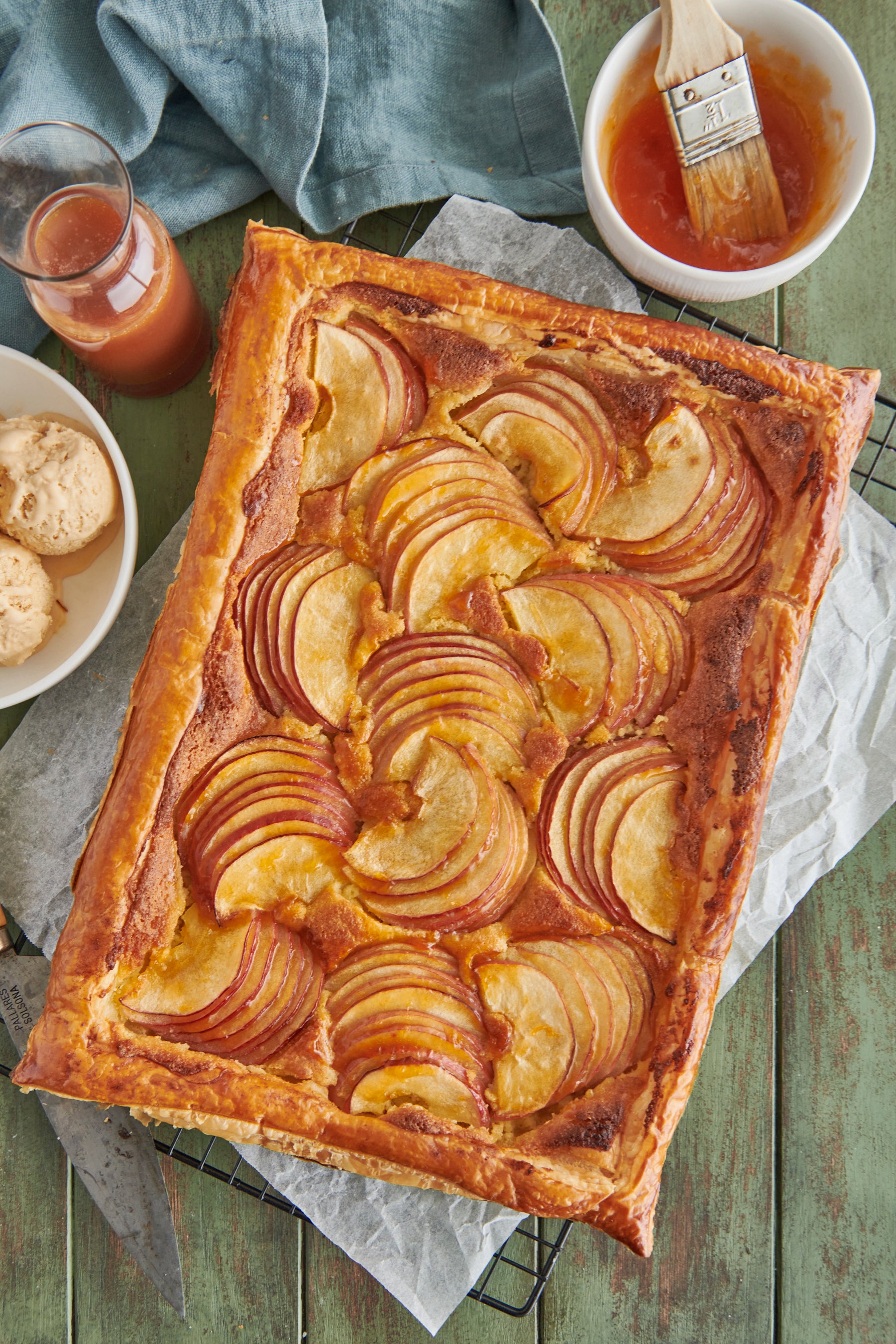 Cooked Apple Galette with a cup of apricot jam and a brush in the top right corner and a jar of caramel sauce and a couple of scoops of ice cream to the left.