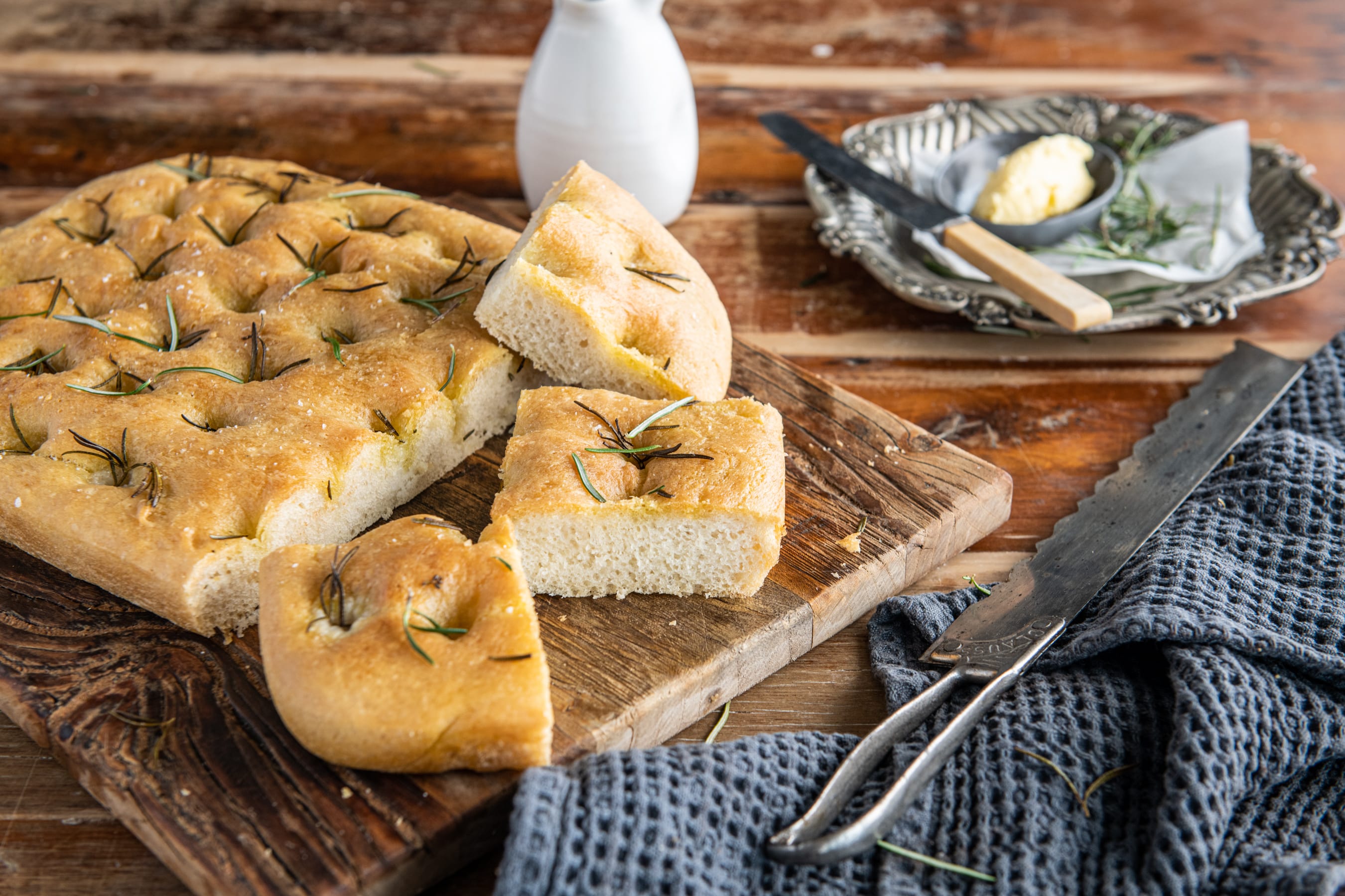 Baked and sliced focaccia with a side plate of butter and rosemary.