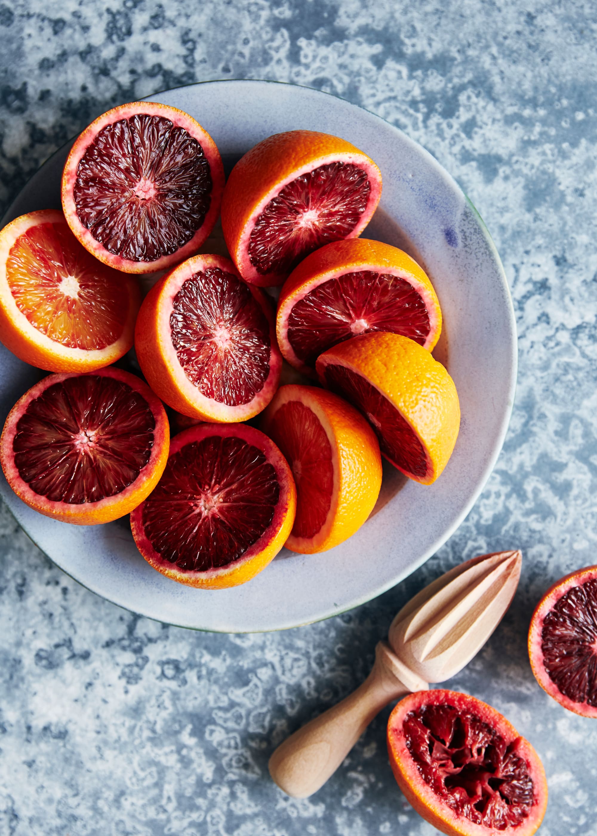 Bowl of cut open blood oranges and a wooden juicer in front of it.