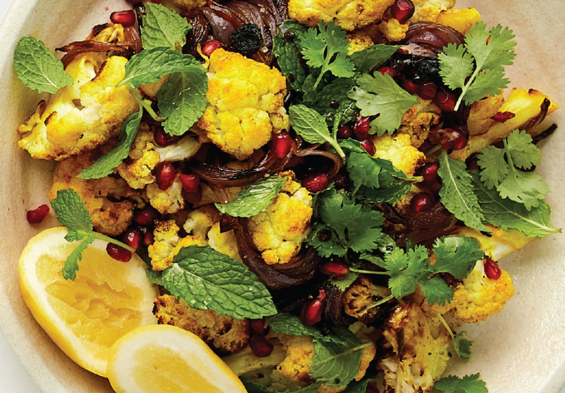 A bowl of warm cauliflower salad with pomegranate seeds, fresh coriander and lemon wedges.