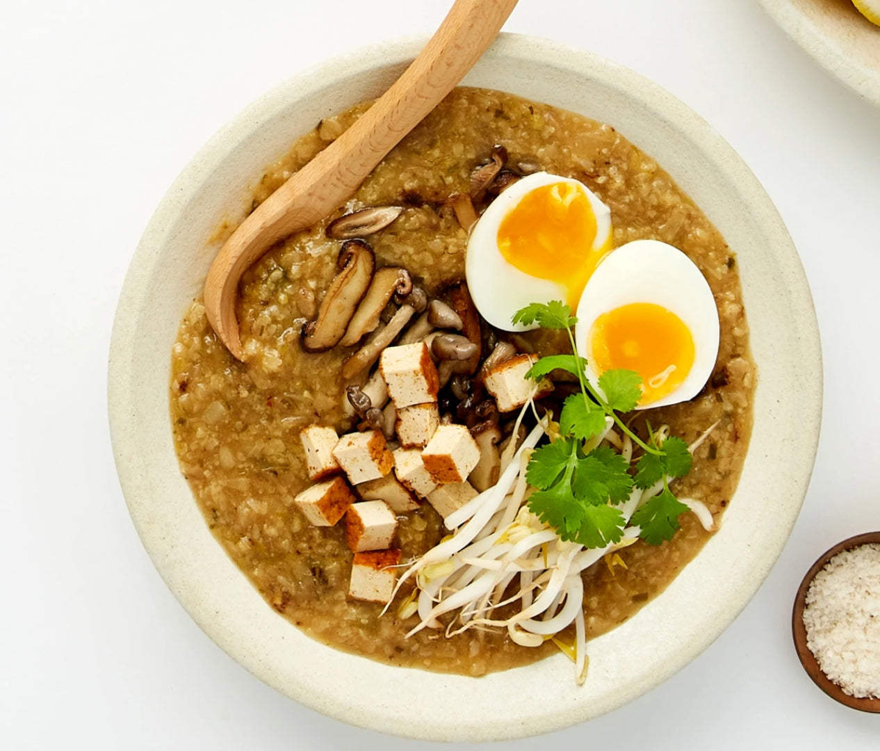 A bowl of caulifower congee topped with a halved boiled egg, diced tofu and bean sprouts