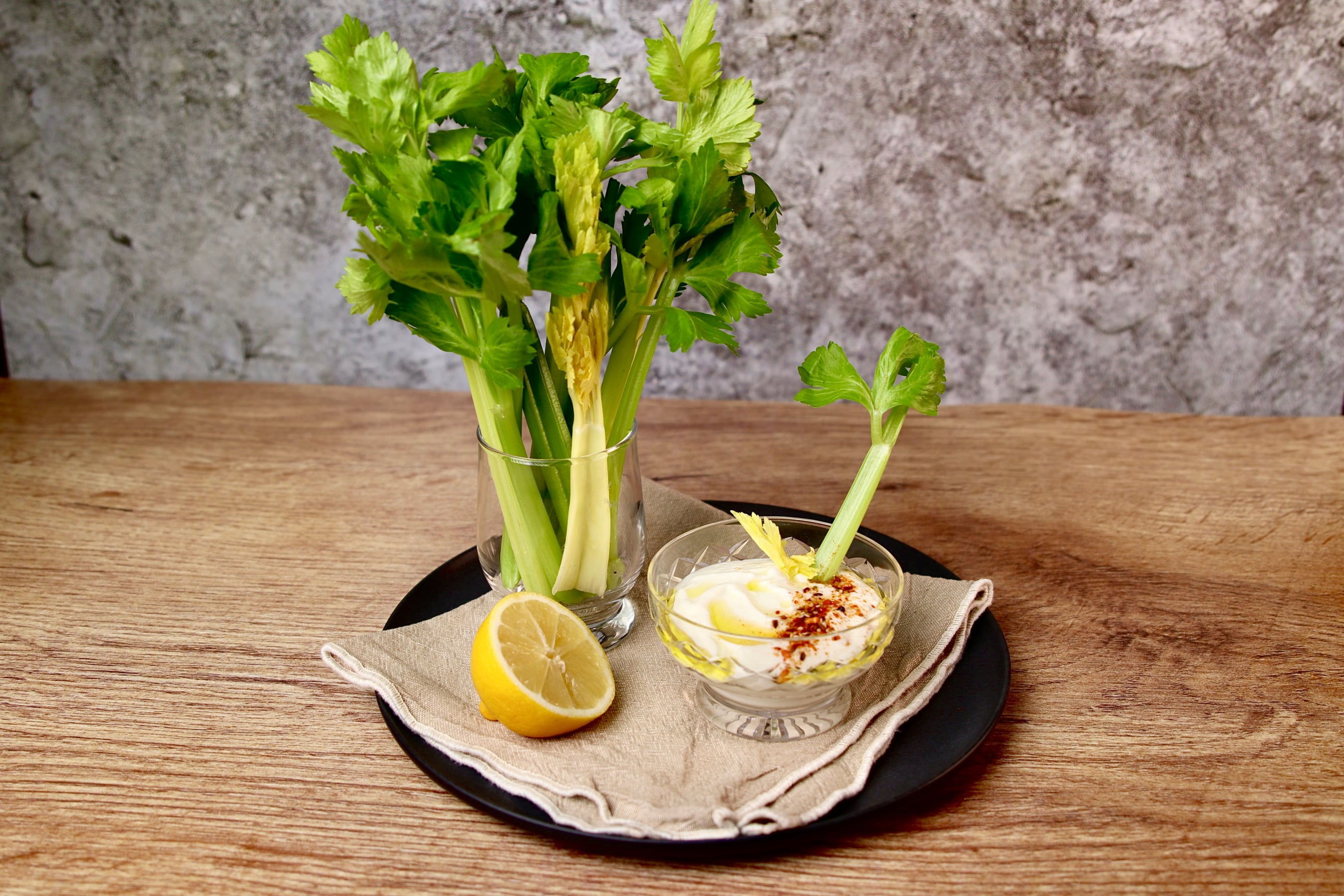 Stalks of celery in a glass with a side of yoghurt garlic dip and half a lemon.