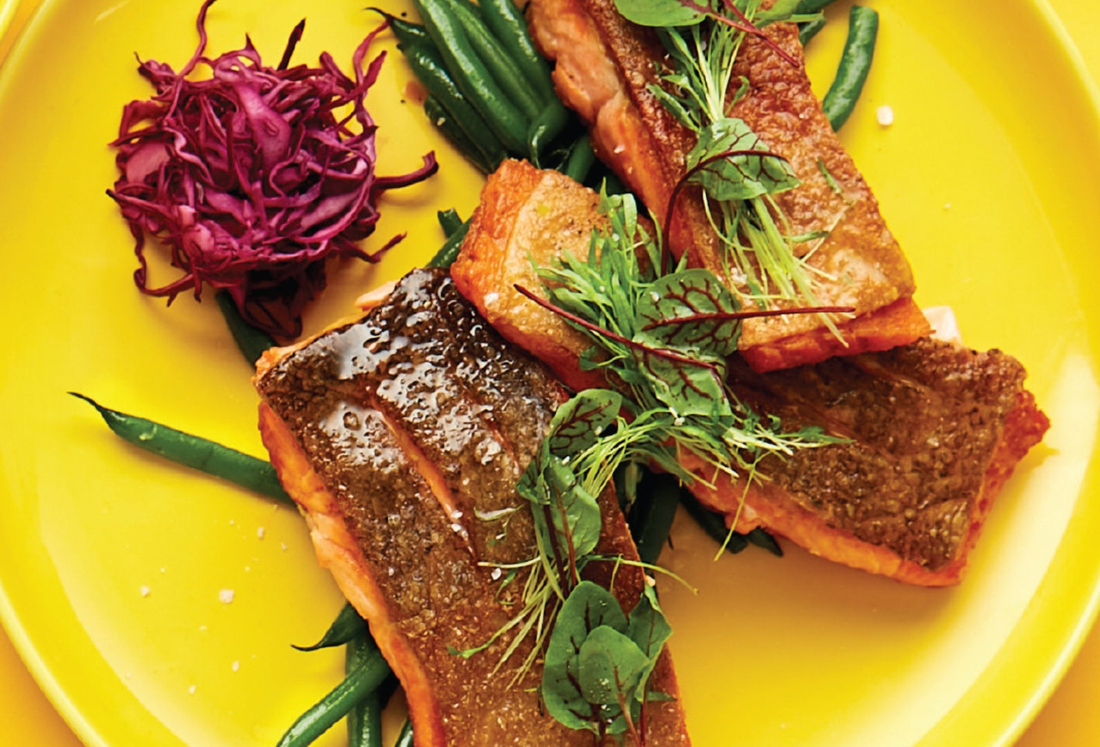 A yellow plate topped with crisp fried salmon, green beans and red cabbage