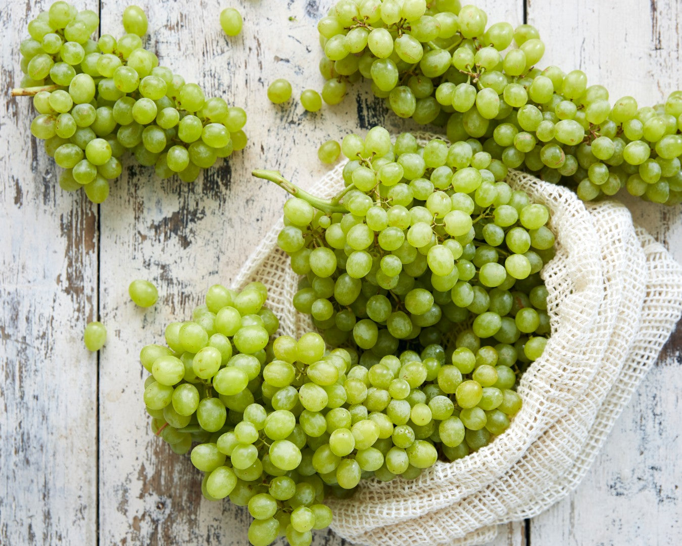 White grapes in a white bag on a white wood background