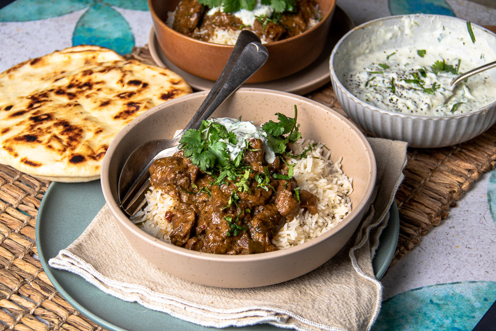 Beef Madras on a bed of rice with a side of naan bread and cucumber raita.