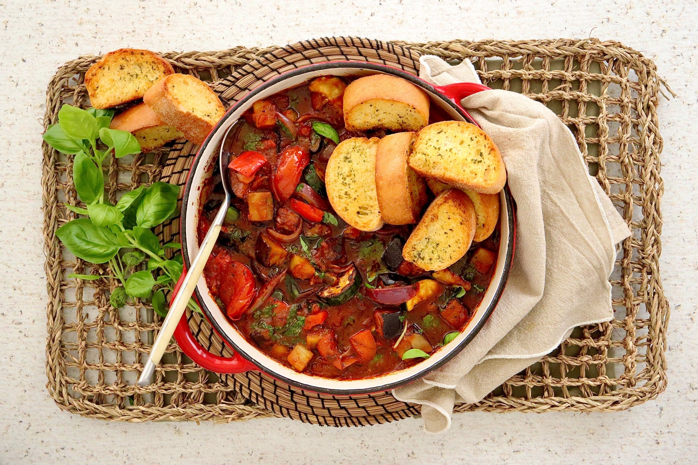 Bowl of ratatouille topped with garlic bread and basil