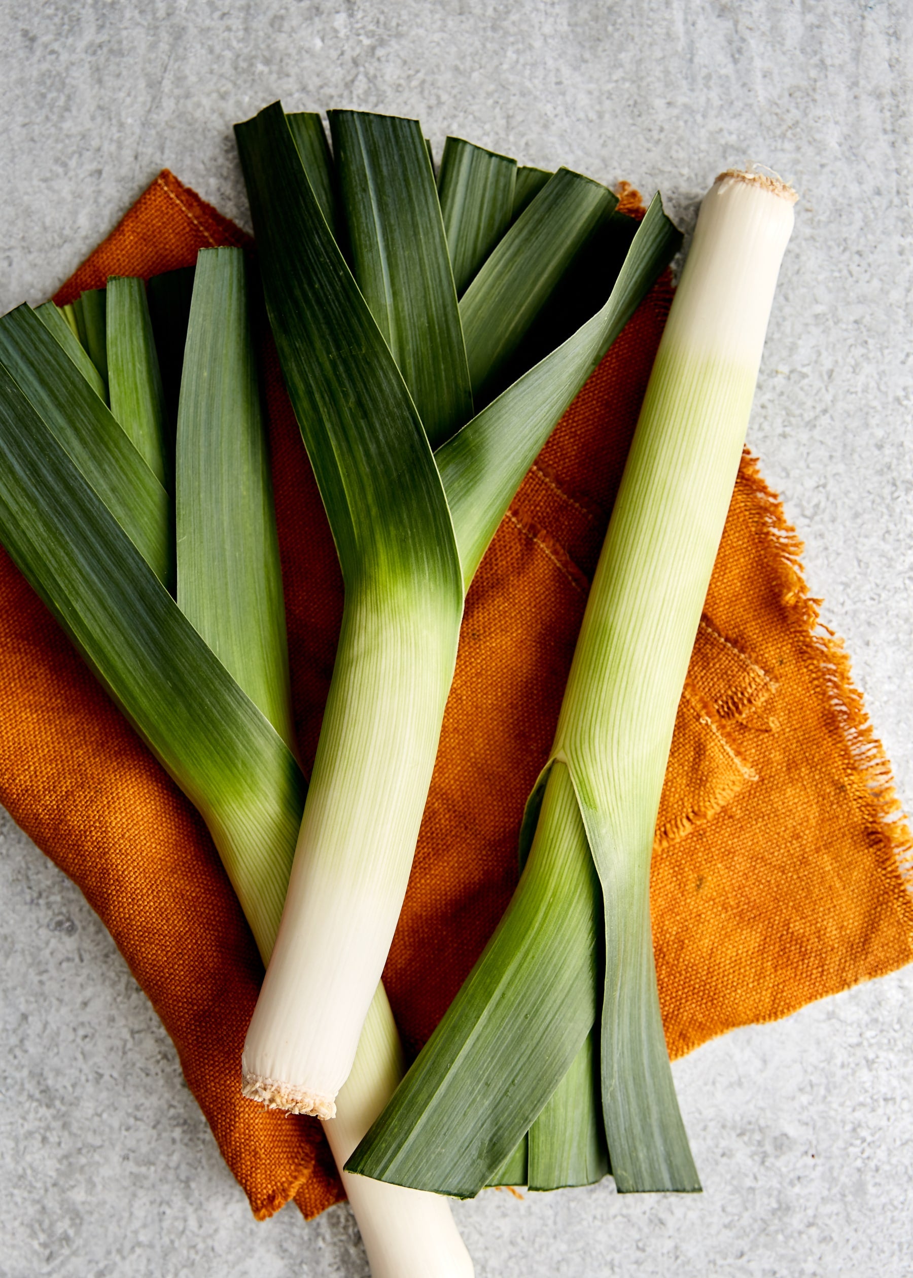 3 whole leeks on a brown cloth on a white bench.