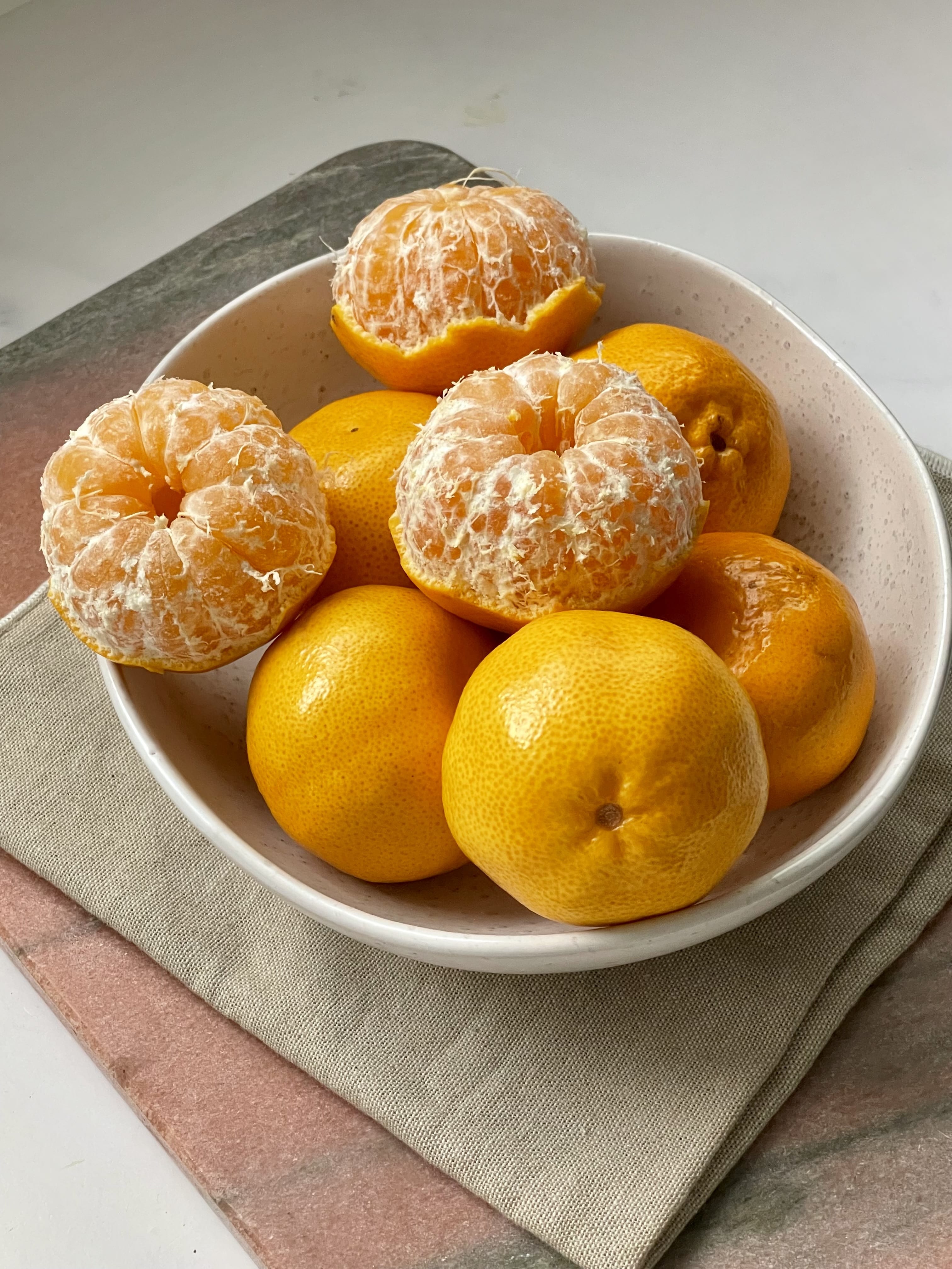 Cream bowl of imperial mandarins with 3 that have been peeled.