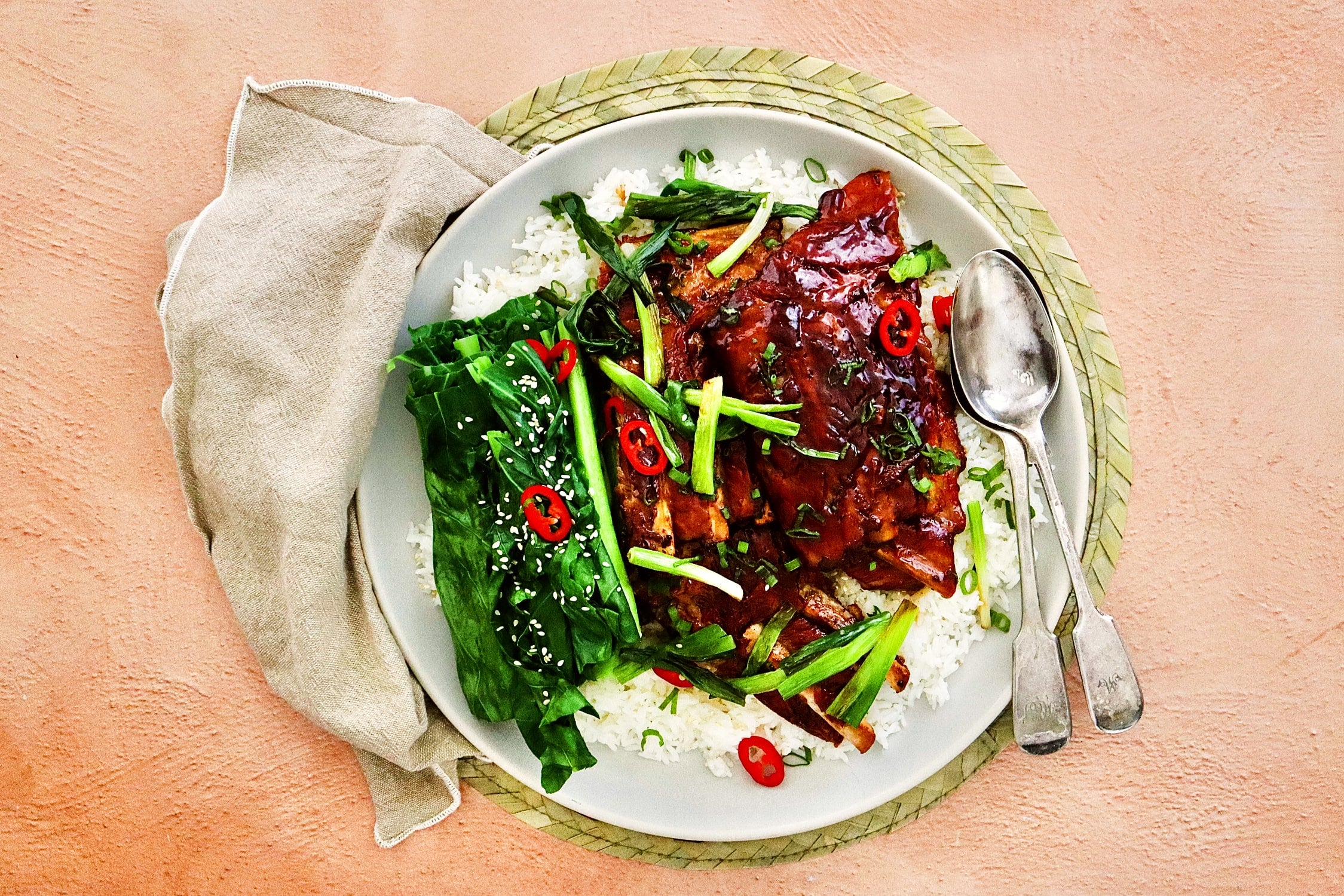 Slow cooked honey soy pork ribs on a bed of rice with a side of gai lan and garnished with sesame seeds and red chilli