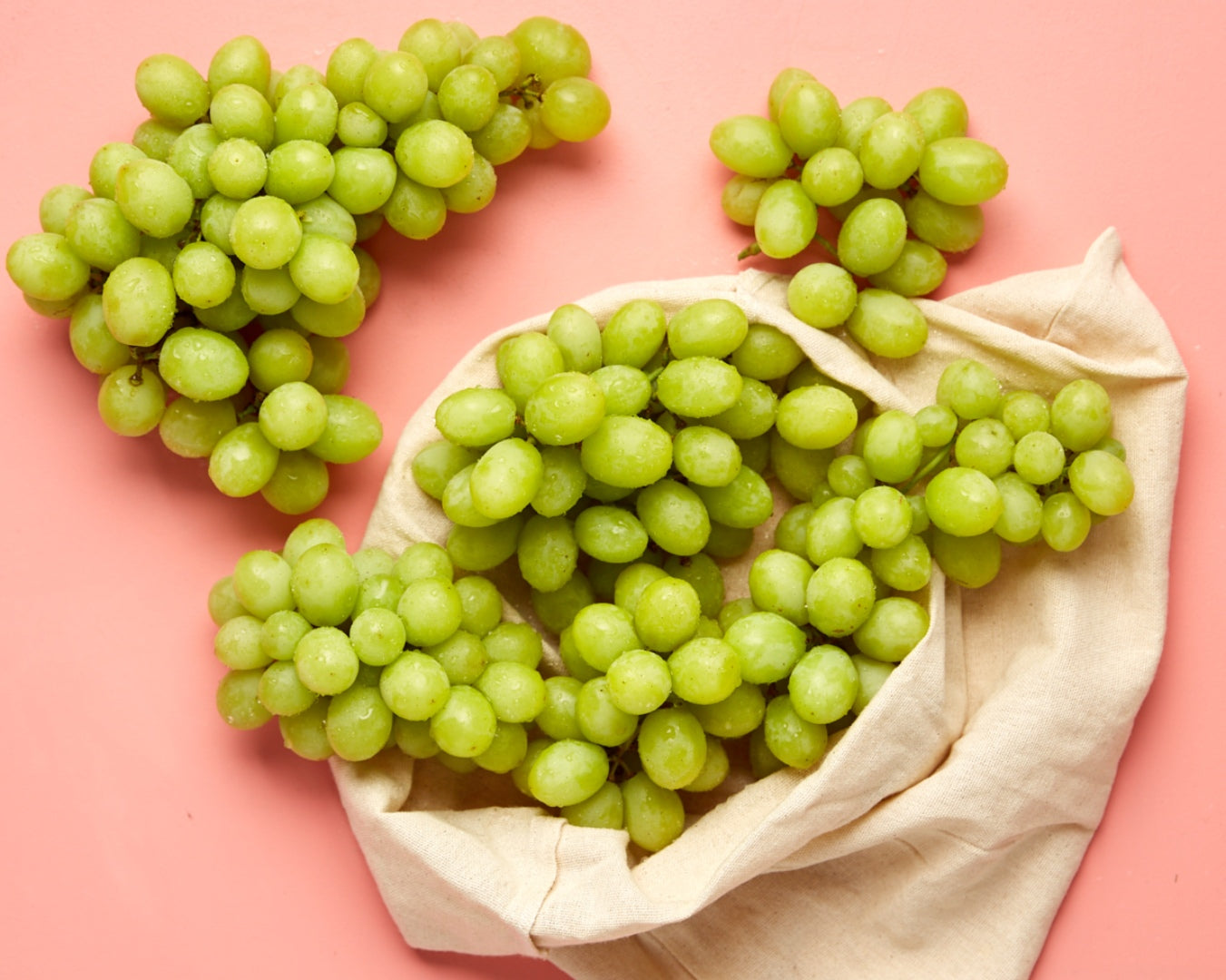 Bunches of Menindee White Seedless Grapes with a net bag on a pink background
